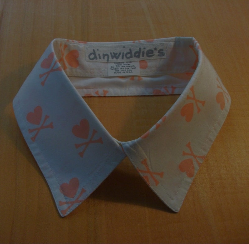 May include: A white cotton collar with a pink and white skull and heart pattern. The collar has a label that reads "dinwiddie's".