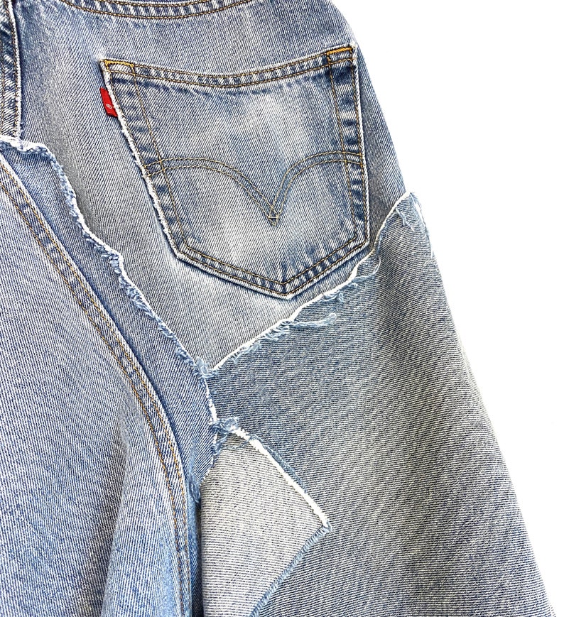 May include: A pair of light blue denim jeans with a distressed look. The jeans have a back pocket with a red tab and stitching around the edges.