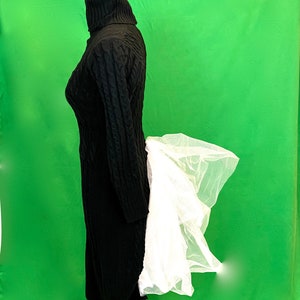 May include: A black turtleneck sweater with a long, cable knit design. The sweater is paired with a white tulle skirt.