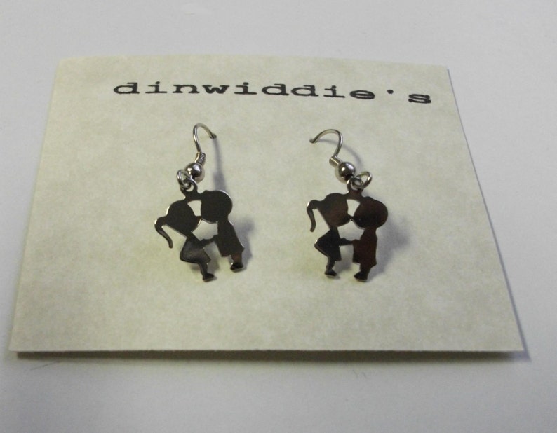 May include: A pair of silver-colored earrings. Each earring features a silhouette of two figures kissing. The earrings are displayed on a cream-colored card with the text "dinwiddie's" printed in black.