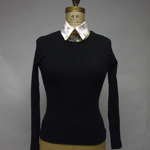 May include: A black long-sleeved ribbed shirt with a white collared shirt underneath. The collared shirt has a pattern of small brown hearts.