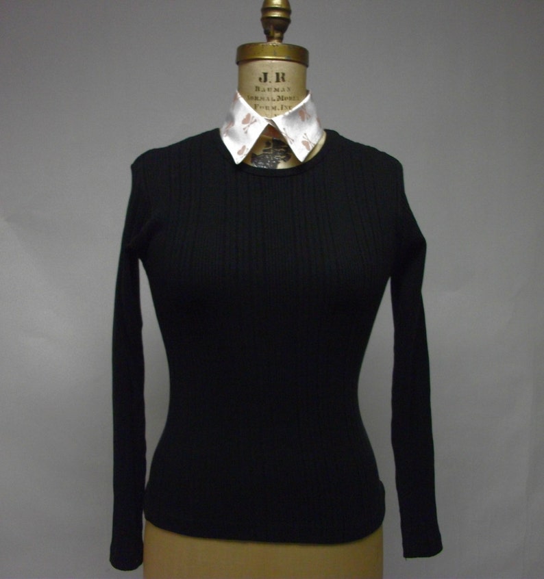 May include: A black long-sleeved ribbed shirt with a white collared shirt underneath. The collared shirt has a pattern of small brown hearts.