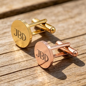 Op de afbeelding: Twee ronde manchetknopen, één in een gepolijste goudtint en één in een gepolijste roségoudtint, elk voorzien van de gegraveerde letters JBD op de ronde voorzijde en een standaard draaimechanisme aan de achterzijde voor bevestiging.