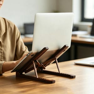 Può includere: Un supporto per laptop in legno marrone scuro con telaio regolabile e un laptop argentato appoggiato sopra. Il supporto presenta un design a doghe con diverse tacche per la regolazione dell'altezza, offrendo una superficie inclinata.