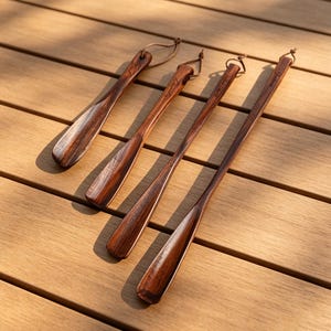 Könnte beinhalten: Vier dunkelbraune Schuhanzieher aus Holz in verschiedenen Längen, jeder mit einer glatten, polierten Oberfläche mit sichtbarer Holzmaserung und einer kleinen Lederschlaufe am Griff zum bequemen Aufhängen und Verstauen.