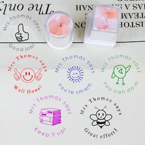 Könnte beinhalten: Eine Sammlung farbenfroher Stempel mit positiven Botschaften wie "Good job!" und "Well Done!". Die Stempel zeigen Illustrationen eines Daumens nach oben, eines Smiley-Gesichts, einer Sonne, eines Vogels, von Büchern und einer Biene. Der Text "Mrs. Thomas says" ist enthalten.