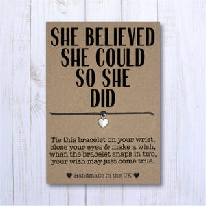 May include: A brown card with the text "SHE BELIEVED SHE COULD SO SHE DID" and a black string bracelet with a silver heart charm. The card also includes instructions for making a wish with the bracelet. The card is handmade in the UK.