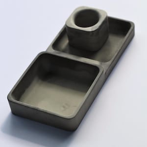 May include: A gray concrete desk organizer with three compartments. The organizer features a square cup holder and two rectangular trays. The design is minimalist and modern, suitable for office or home use.