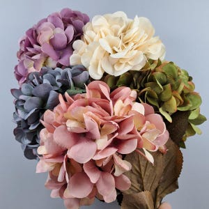 Peut inclure: Un bouquet d'hortensias artificiels dans des tons de violet, bleu, rose et vert. Les fleurs sont disposées en grappe avec des feuilles brunes.