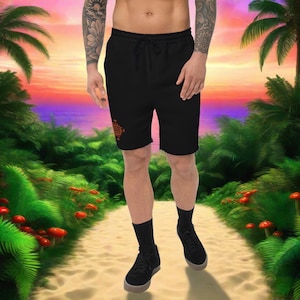 May include: Black athletic shorts with a geometric design in orange on the left leg. The shorts have a drawstring waistband and are worn by a person standing on a path.