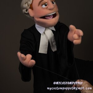 May include: A hand puppet dressed as a lawyer with a white collar and a white barrister's band. The puppet has a brown wig, brown eyes, and a pink tongue sticking out. The puppet is holding a black string in its right hand. The text '@MYCUSTOMPUPPET mycustompuppet@gmail.com' is visible in the bottom right corner of the image.
