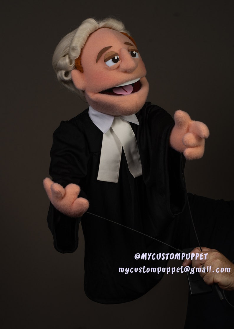 May include: A hand puppet dressed as a lawyer with a white collar and a white barrister's band. The puppet has a brown wig, brown eyes, and a pink tongue sticking out. The puppet is holding a black string in its right hand. The text '@MYCUSTOMPUPPET mycustompuppet@gmail.com' is visible in the bottom right corner of the image.