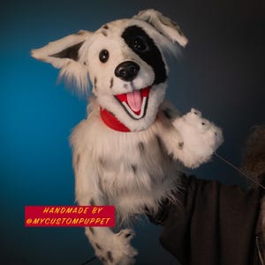 May include: A handmade Dalmatian dog puppet with a red collar. The puppet has black spots, a black patch over one eye, and a pink tongue. The text "HANDMADE BY @MYCUSTOMPUPPET" is displayed on a red banner.