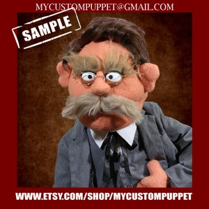 Puede incluir: Una marioneta hecha a mano con una apariencia distinguida. La marioneta presenta una cara melocotón claro, un gran bigote gris y cabello castaño oscuro. Lleva un traje gris, una camisa blanca con cuello y gafas redondas. La palabra "SAMPLE" está estampada en la parte superior izquierda.