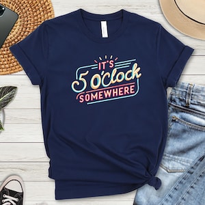 Pode incluir: Uma camiseta azul marinho com um gráfico de estilo retrô que diz "São 5 horas em algum lugar".