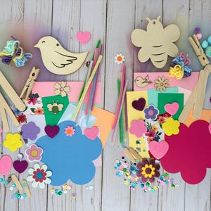 May include: A craft kit with various colorful supplies, including wooden bird and bee shapes, pipe cleaners, felt hearts, flowers, sequins, and craft sticks. The kit is arranged on a light wood-grain surface, perfect for creative projects.
