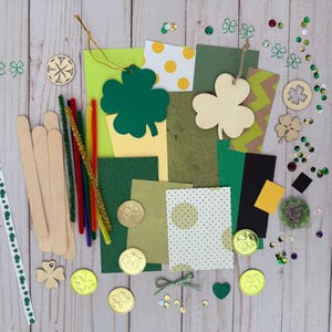 May include: A collection of St. Patrick's Day craft supplies, including green shamrock cutouts, gold coins, pipe cleaners, wooden craft sticks, and decorative paper. The items are arranged on a light wood surface.