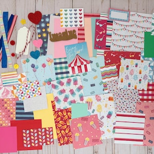 May include: A collection of colorful scrapbook paper, ribbons, and embellishments. The papers feature various patterns, including balloons, ice cream, and circus themes. Decorative elements include felt hearts, buttons, and the word "Imagine".