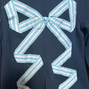 May include: A dark blue blazer with a large white and light blue striped bow on the back.