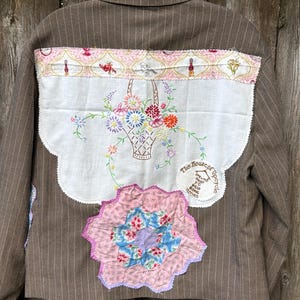 May include: A brown pinstriped blazer featuring a large white embroidered panel on the back with a floral basket design, a pink patterned border, and a circular patch that reads The House of Upcycle Life is too short to wear boring clothes.