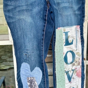 May include: Blue denim jeans with patches of fabric sewn on. The patches include a heart, floral patterns, and the word "LOVE" in teal.