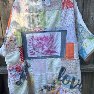May include: A patchwork jacket with a variety of fabric patterns and colors, including floral, paisley, and solid patches. The jacket features a pink cupid graphic and the text "love". The label reads "The House of Upcycle".