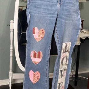 May include: Blue denim jeans with patchwork hearts and the word "LOVE" sewn on the leg.