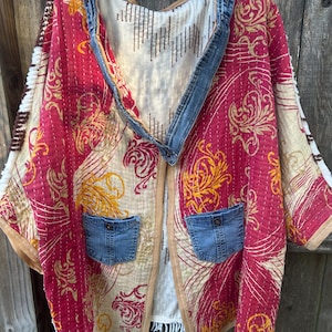 May include: A quilted jacket with a red and gold floral pattern, denim accents, and two denim pockets. The jacket has a cream-colored lining and a brown trim. The sleeves are wide and the jacket is open in the front.