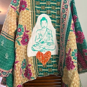 May include: A patchwork jacket with a Buddha image and an orange heart. The jacket features floral patterns in shades of green, purple, and yellow. The design includes a white Buddha image and an orange heart, adding a spiritual and artistic touch to the garment.