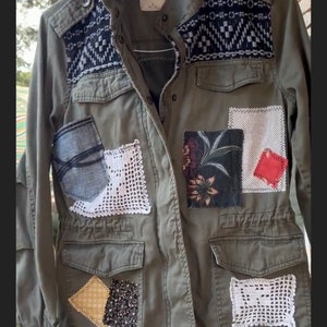 May include: A green utility jacket with various patches sewn on. The patches include floral fabric, crocheted squares, and a denim pocket. The jacket has a label that reads "Mudd".