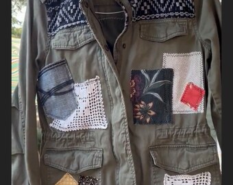 May include: A green utility jacket with various patches sewn on. The patches include floral fabric, crocheted squares, and a denim pocket. The jacket has a label that reads "Mudd".