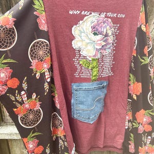 May include: A maroon long-sleeved shirt with a large floral graphic and a denim pocket. The sleeves feature a brown fabric with dreamcatcher and floral patterns. Text on the shirt reads "WHY ARE YOU OK TOUR 2016".
