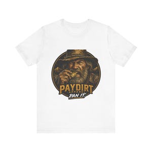 Può includere: Una t-shirt bianca a maniche corte con una grafica circolare di un cercatore d'oro barbuto con cappello che tiene in mano una pepita d'oro. Il testo PAYDIRT APPAREL PAN IT è stampato in lettere dorate e bianche nel design circolare.