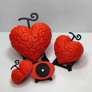 Op de afbeelding: Drie rode hartvormige decoratieve dozen met een swirl-patroon. De dozen zijn gemaakt van plastic en hebben een zwarte standaard. De grootste doos heeft een zwarte steel met een krul aan de bovenkant.