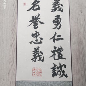Peut inclure: Un rouleau asiatique traditionnel avec calligraphie noire sur fond crème. Le rouleau présente des bordures grises décoratives et un rouleau en bois marron foncé. Le texte est en colonnes verticales.