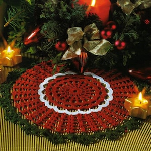 May include: A handmade, red crocheted doily with a white scalloped border and green trim. The doily is placed on a table with a Christmas theme, surrounded by candles, ornaments, and greenery.
