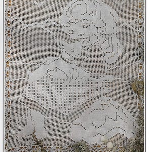 May include: A white, open-weave crochet doily featuring a detailed floral design. The intricate pattern is bordered with a scalloped edge. The doily is placed on a wooden surface, with decorative elements like small stones and dried plants.