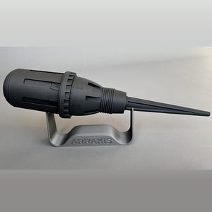 May include: A black 3D printed model of a futuristic weapon, labelled "ARRAKIS", on a stand.