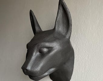 May include: A dark gray, 3D-printed sculpture of a dog's head, mounted on a wall. The sculpture has detailed features, including pointed ears and a defined snout. The text "DIGITAL FILE FOR 3D PRINTING" is at the top of the image.