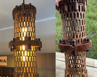 May include: A 3D printed metal lamp with a rusty finish. The lamp is made of multiple gears and has a cage-like design. The lamp is lit and casting a warm glow.