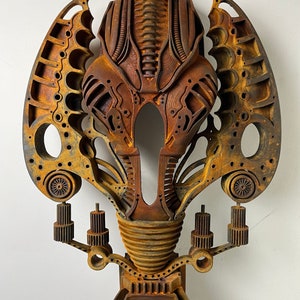 May include: A rusty metal sculpture of a stylized alien head with intricate details and a textured surface. The sculpture is mounted on a base with gears and other mechanical elements.