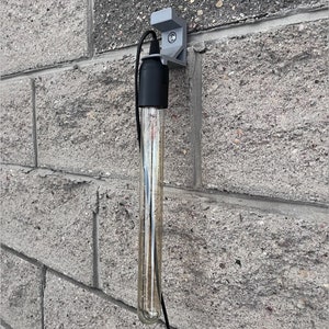 May include: A clear glass tube light bulb with a black cord and a gray wall mount. The light bulb is hanging from the wall mount.