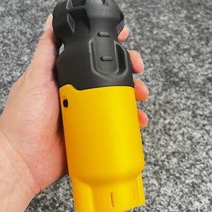 Puede incluir: Un conector eléctrico bicolor negro y amarillo. La parte superior es negra con un diseño texturizado, mientras que la sección inferior es de color amarillo brillante. El conector se sostiene en una mano sobre un fondo gris.