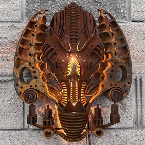 May include: A rusty metal wall sculpture in the shape of a face with intricate details and a glowing orange light in the center.