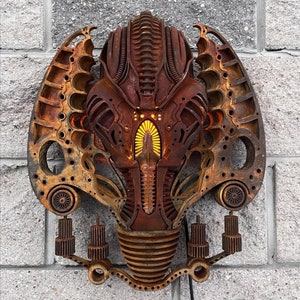 May include: A rusty metal wall sculpture in the shape of a face with intricate details and glowing lights. The sculpture is mounted on a brick wall.