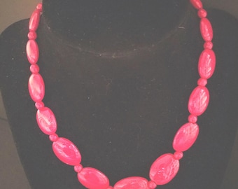 Peut inclure: Un collier rose vif présenté sur un mannequin noir. Le collier est composé de grandes perles ovales alternant avec de petites perles rondes. Les perles ont une finition brillante. Un bijou audacieux.