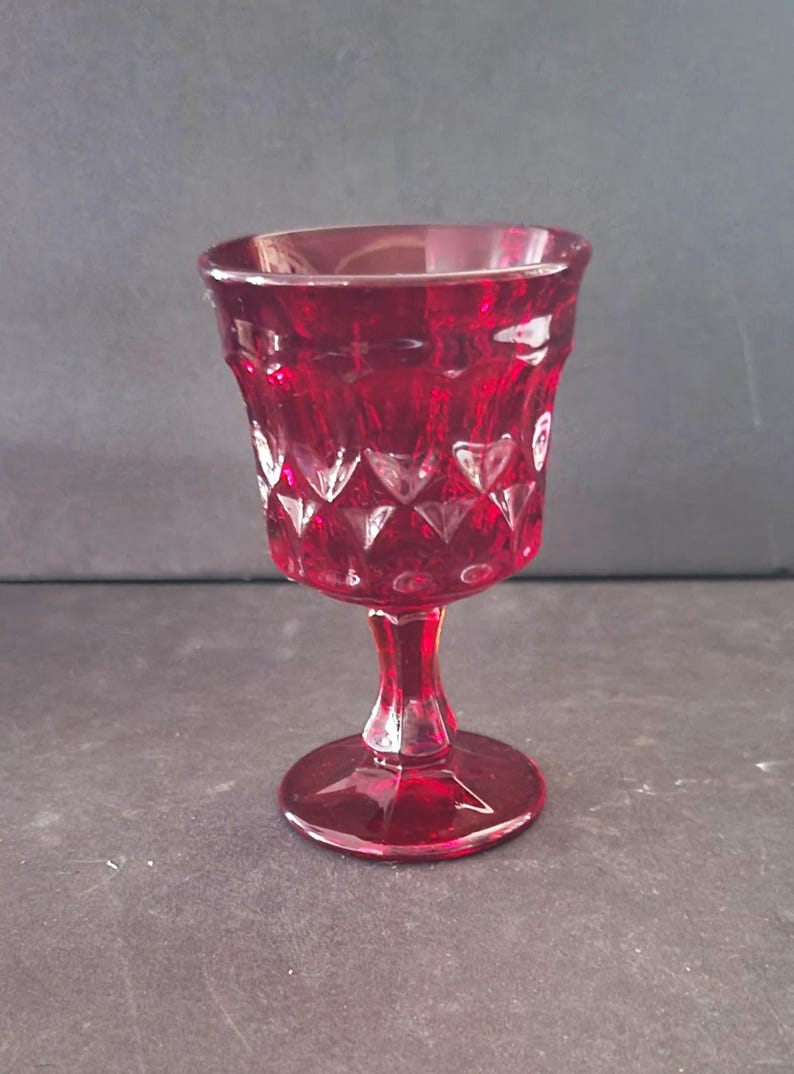 Op de afbeelding: Een robijnrode glazen kelk met een diamant- en hartpatroon. De steel en voet zijn ook rood. De kelk wordt waarschijnlijk gebruikt voor het serveren van wijn of andere dranken. Het glas heeft een vintage uitstraling.