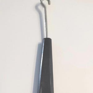 May include: A metal crochet hook with a black, faceted handle. The hook is silver-colored and curved at the end. The handle is a dark, solid color.