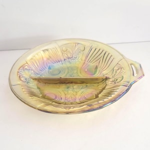 Pode incluir: Uma travessa oval iridescente com interior dividido. A travessa apresenta um padrão decorativo em relevo e duas pequenas pegas. As cores mudam de dourado para azul e roxo, criando um efeito brilhante. Uma peça vintage.