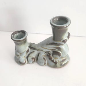 May include: A ceramic candle holder with two openings. The holder is a light blue color with brown accents and a textured design. The openings are a darker shade of blue. The candle holder is a decorative item.